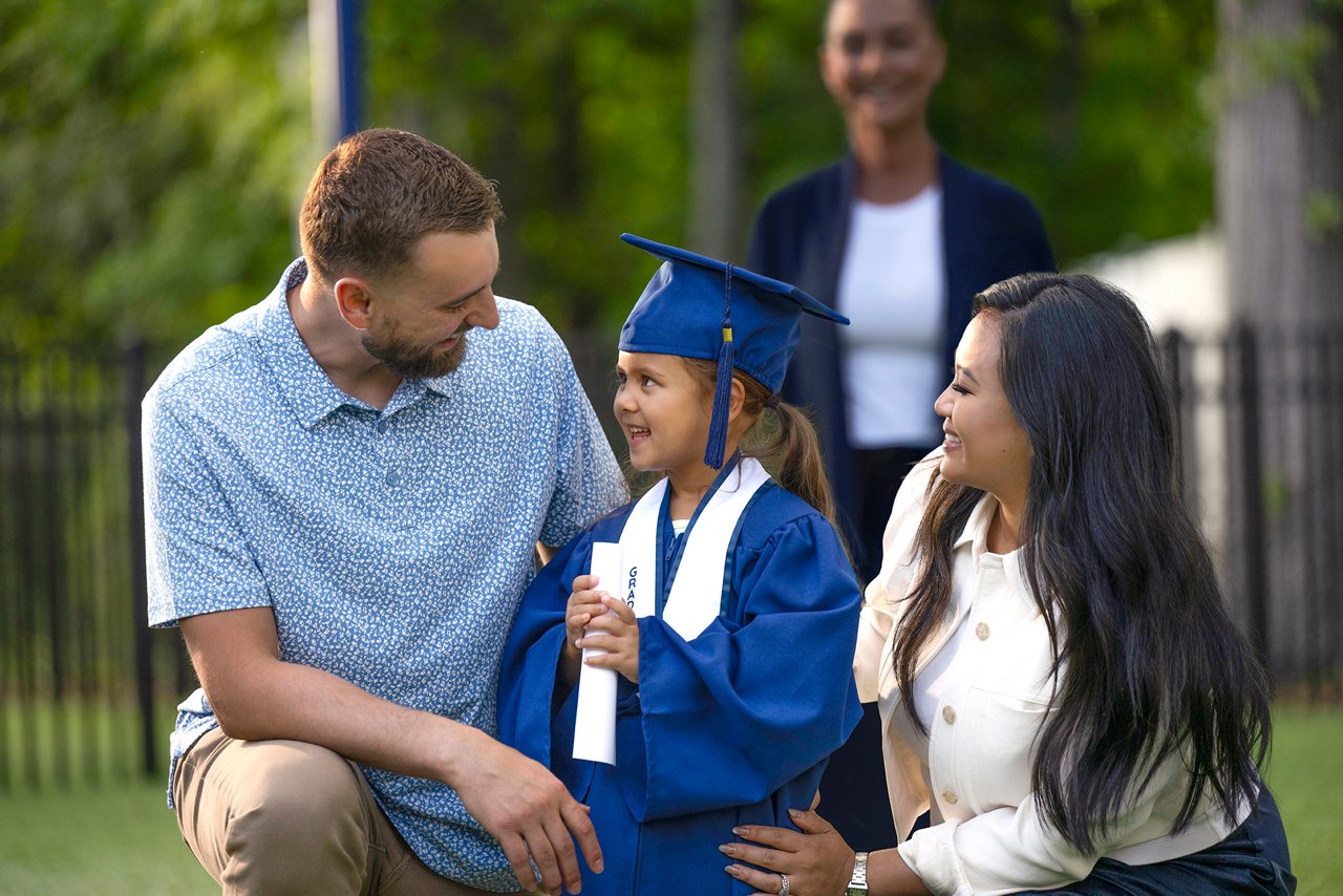 A father and mother smiling at their preschool graduate in cap and gown