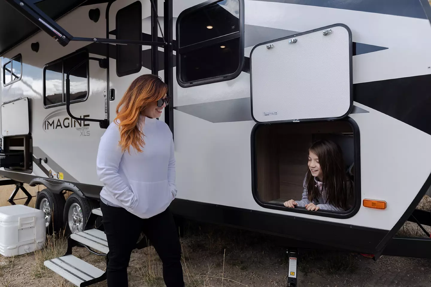 Camper smiling at child who's sitting inside of an RV compartment storage area. 