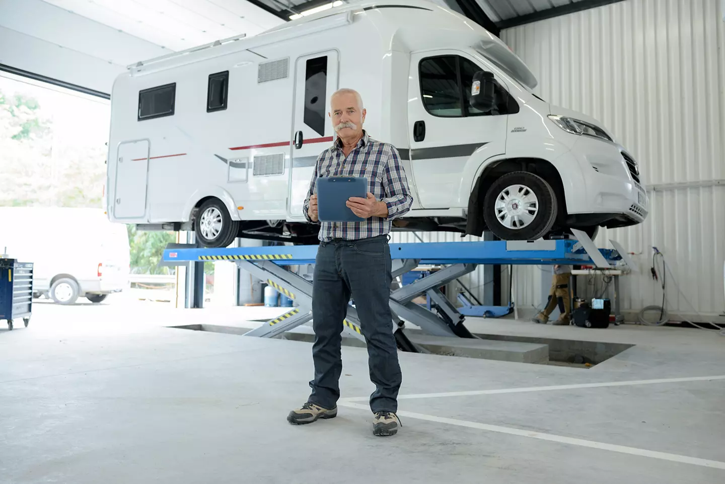 Service technician standing in front of a campervan on a lift. 