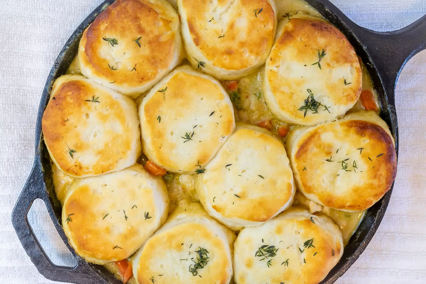 Chicken pot pie covered in biscuits cooked in a cast iron skillet.