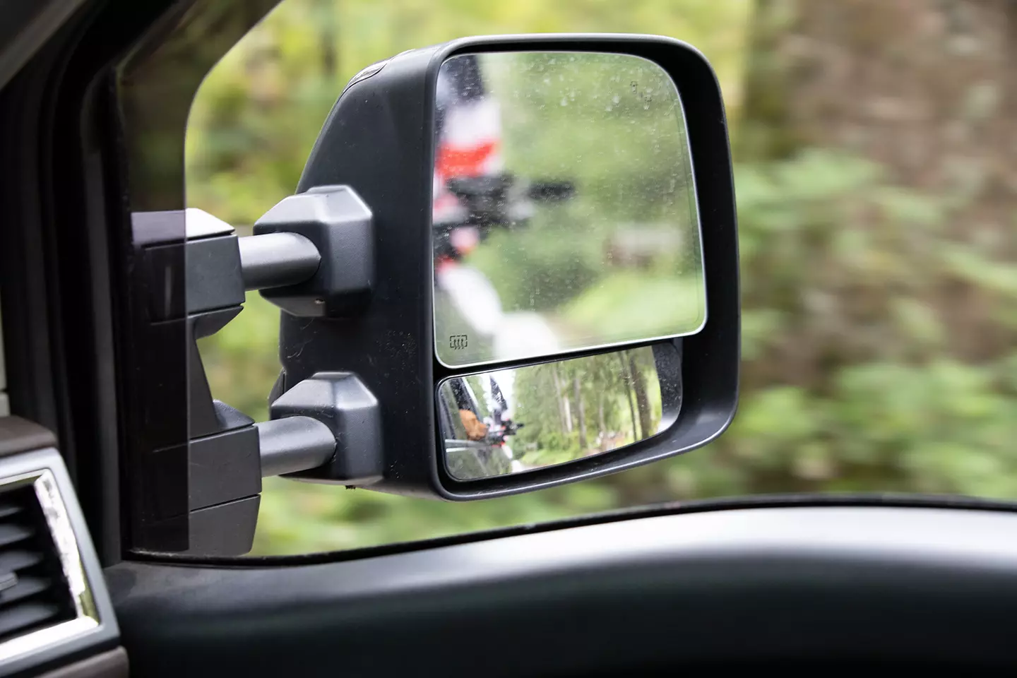 Extended rear view mirror with a blurry reflection of a dog sitting in the backseat of a truck. 