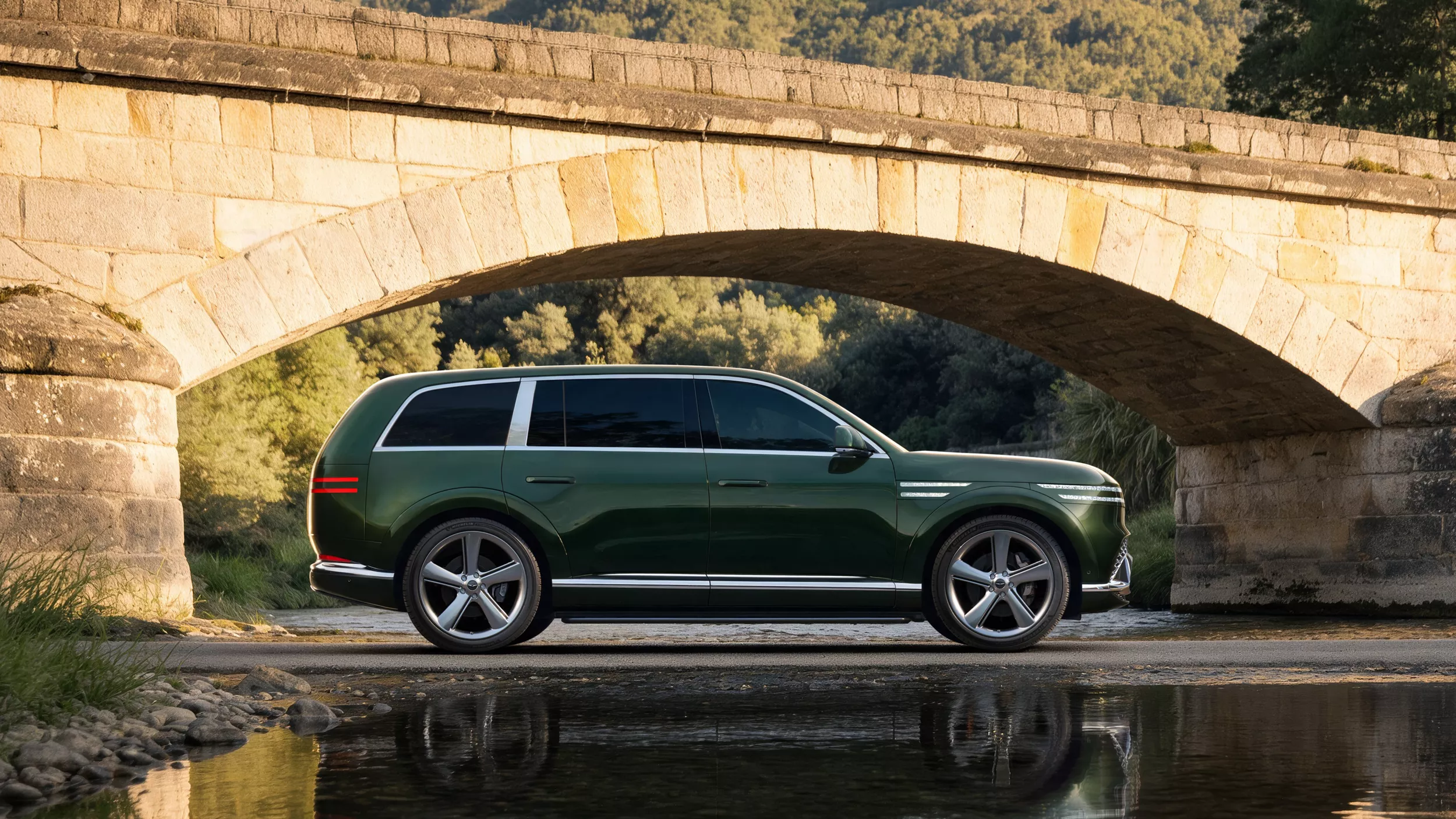 Driver-side profile view of 2028 Genesis GV90 in Baena Green parked beside a reflecting pool