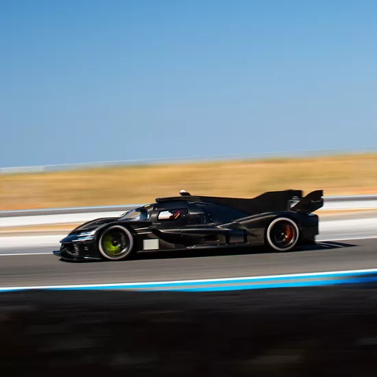 Driver-side profile view of Genesis Magma Racing GMR-001 Hypercar in black, driving along race track