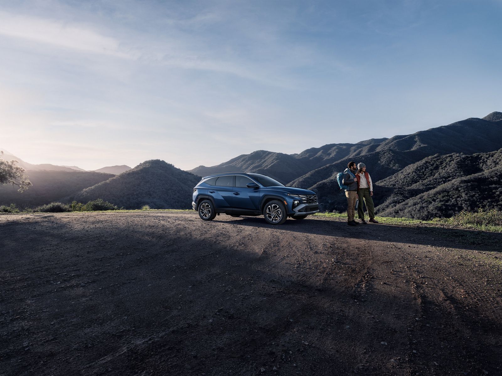 Blue gas Hyundai Tucson parked at a mountain overlook with two people standing beside it
