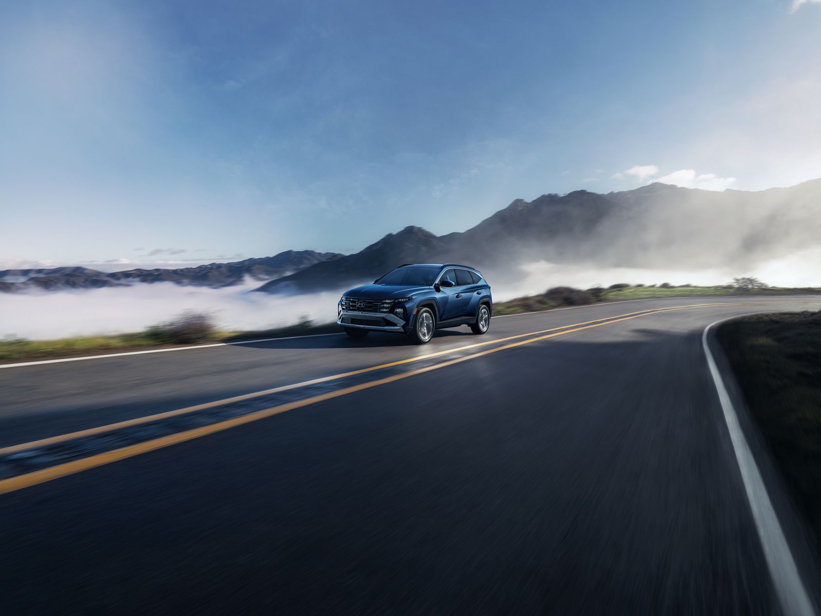 Blue Hyundai Tucson Hybrid driving on a winding mountain road above the clouds