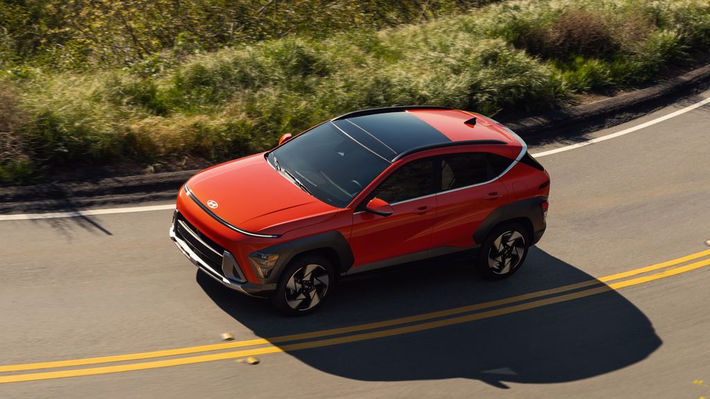 Orange Hyundai Kona with a black roof driving on a curving two-lane road, seen from above