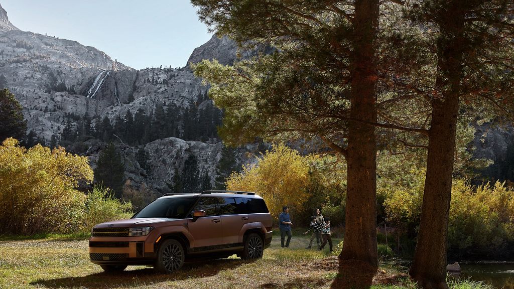 Copper Hyundai Santa Fe parked in a grassy clearing below granite mountains while a family walks among pine trees