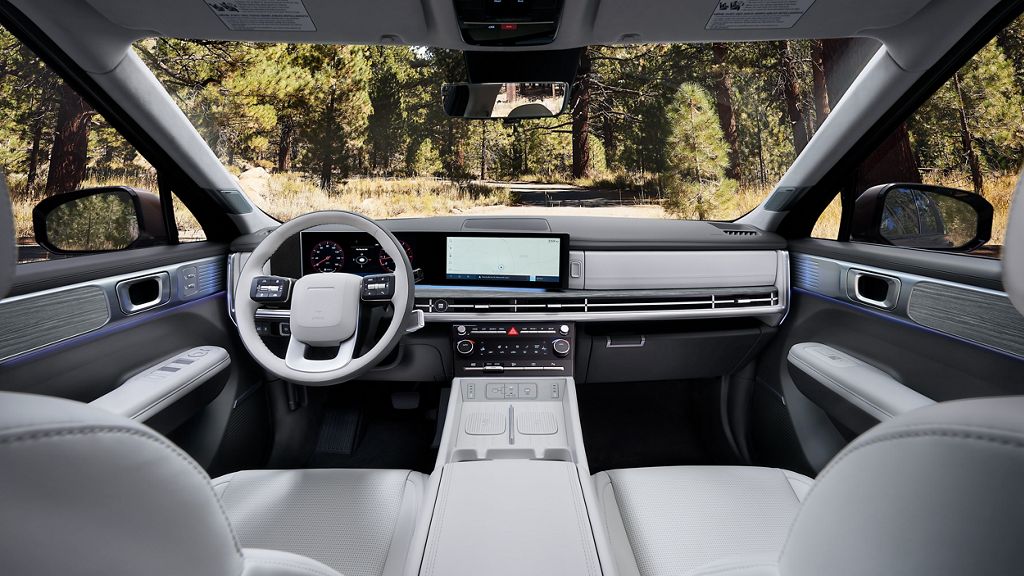 Hyundai Santa Fe dashboard and front seats in light gray, with the steering wheel, center screen and climate controls in view and trees outside the windshield