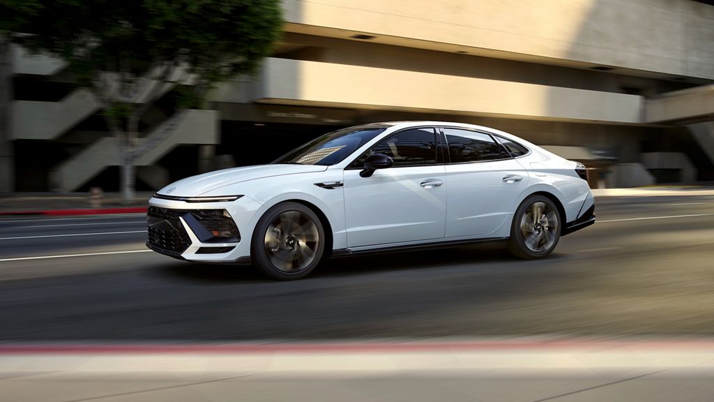 White Hyundai Sonata sedan driving past a concrete building on a city street