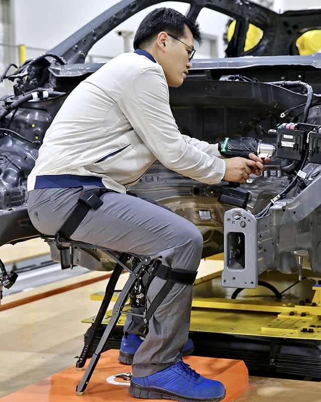 Hyundai employee sitting with a Hyundai Chairless Exoskeleton as he works on a car