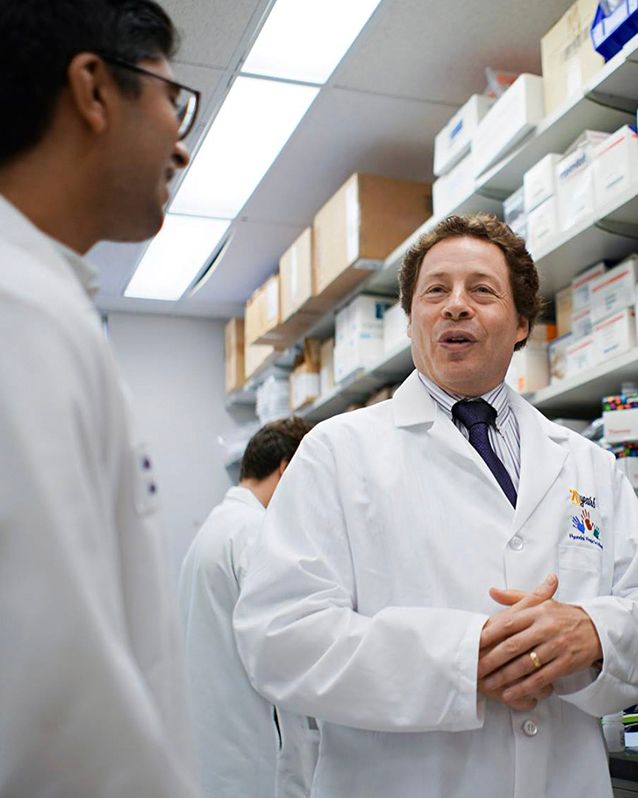 Two male doctors wearing Hope On Wheels lab coats talk to each other and smile inside their lab