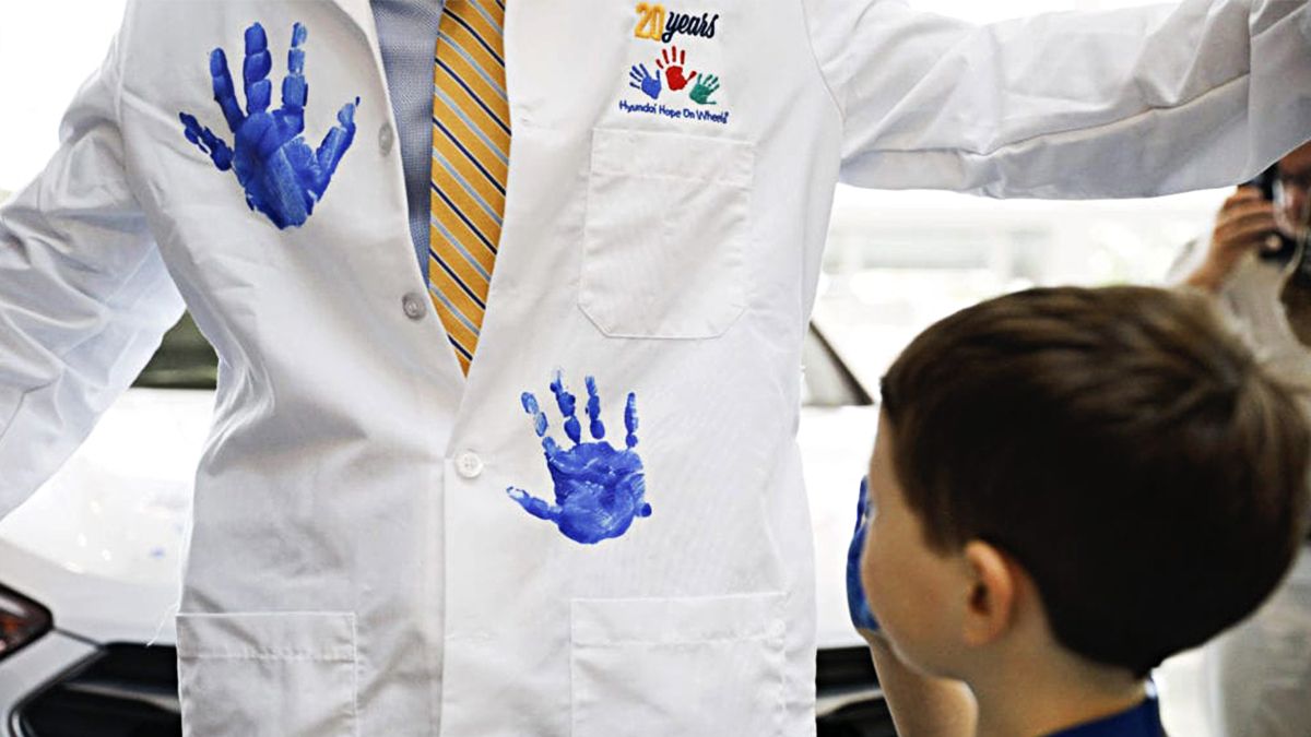 Doctor has blue handprints stamped on his lab coat by a young patient.