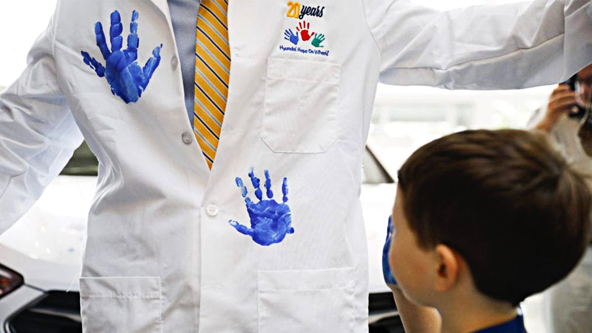 Doctor has blue handprints stamped on his lab coat by a young patient.