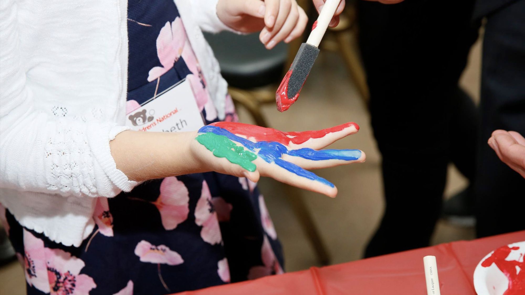 Embajadora juvenil se pone pintura roja, azul y verde en la mano en un evento de Hope On Wheels