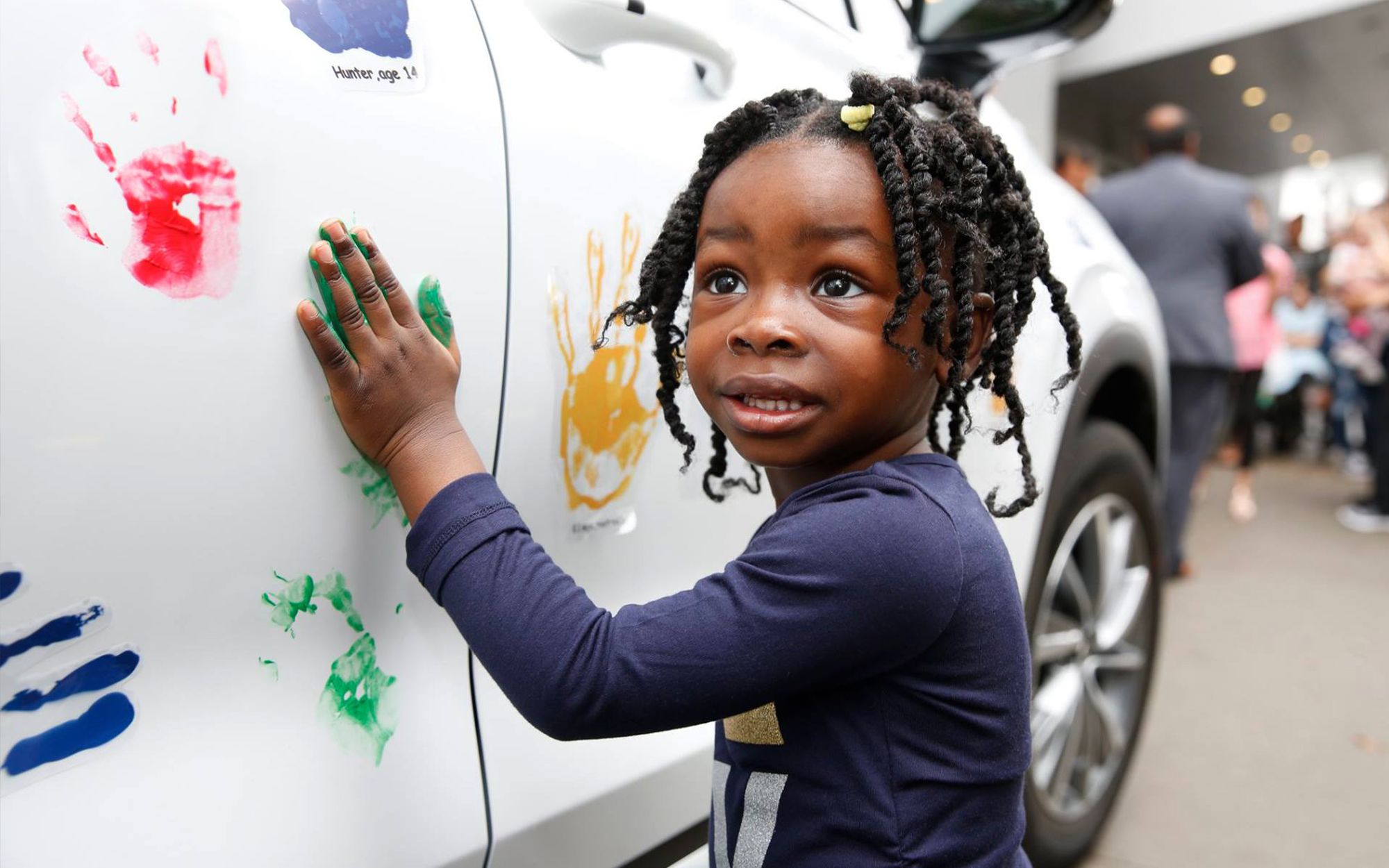 Little girl stamps her handprint with green paint on a Hyundai car during a Hope on Wheels event