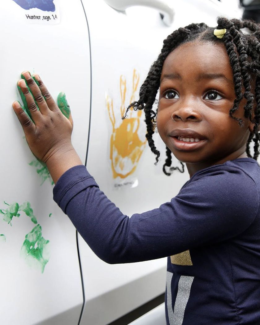Little girl stamps her handprint with green paint on a Hyundai car during a Hope on Wheels event