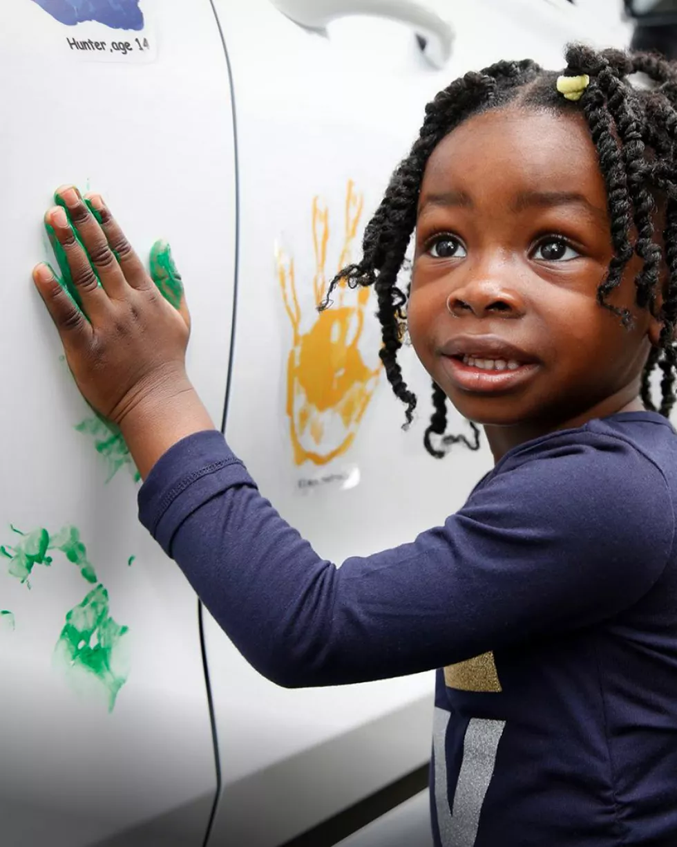 Little girl stamps her handprint with green paint on a Hyundai car during a Hope on Wheels event