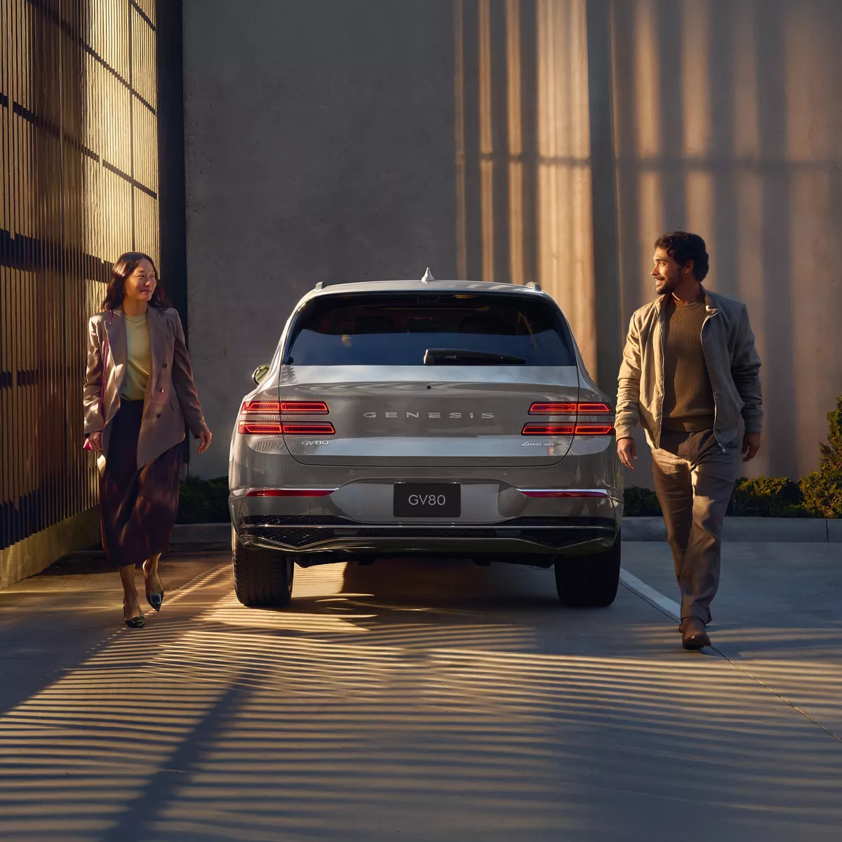 Rear view of Genesis GV80 parked beside modern home with man and woman walking besides vehicle