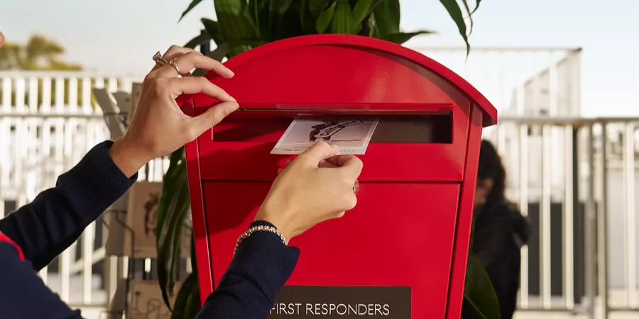 Close up of Alexandra O'Laughlin's hand placing California Rises postcard into mailbox at Genesis Invitational Lounge