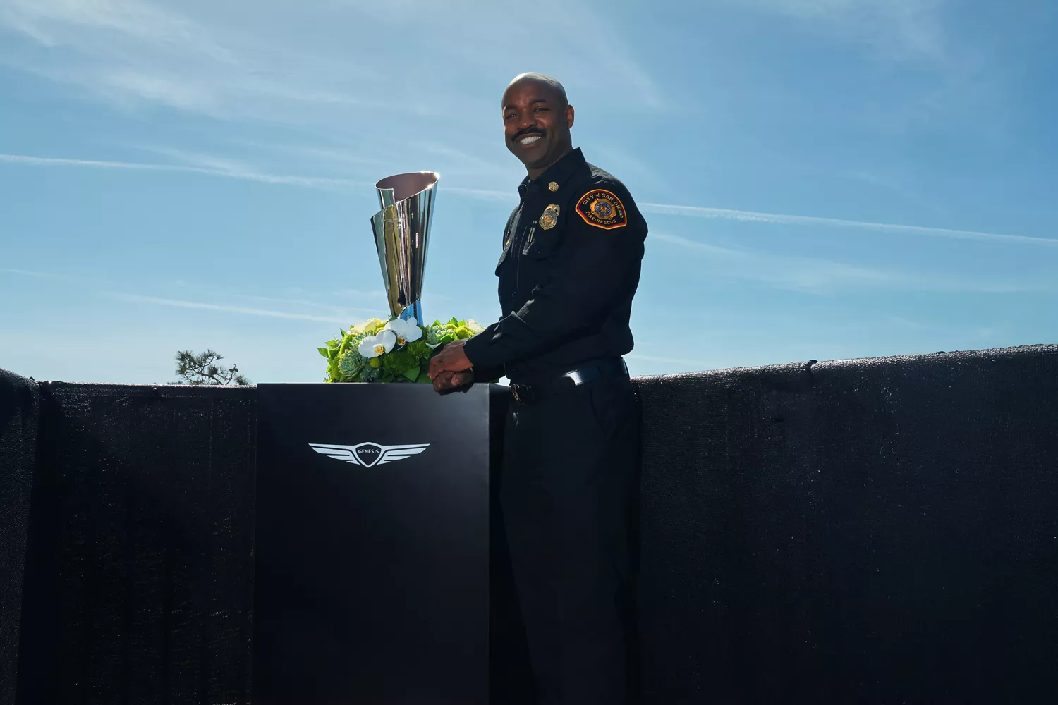 Firefighter standing next to Genesis Invitational trophy at Genesis Invitational, fairway in back