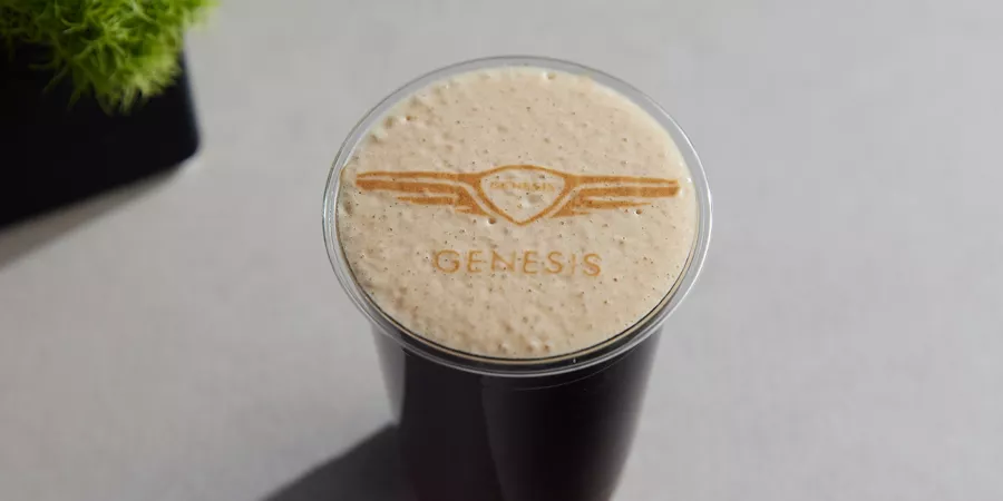 Dark beverage in full glass with Genesis logo etched into frothy foam on top