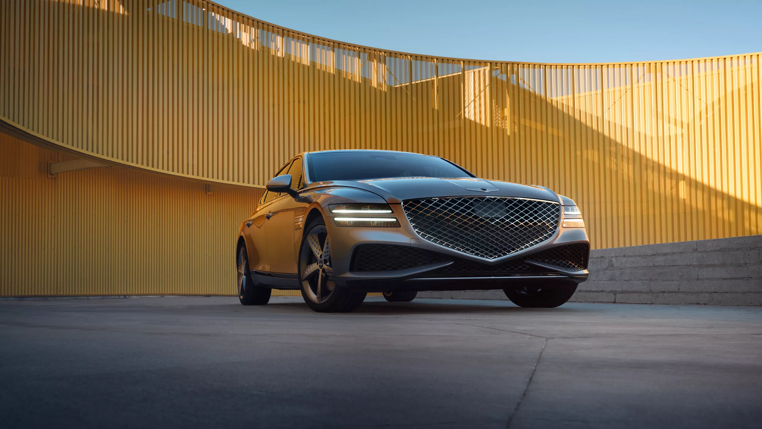 Front view of a gray 2025 Genesis G80 parked in front of a yellow paneled wall