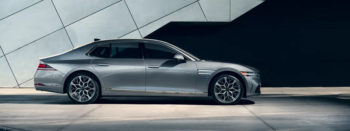 Exterior passenger side profile view of 2026 Genesis G90 in Savile Silver next modern metal building