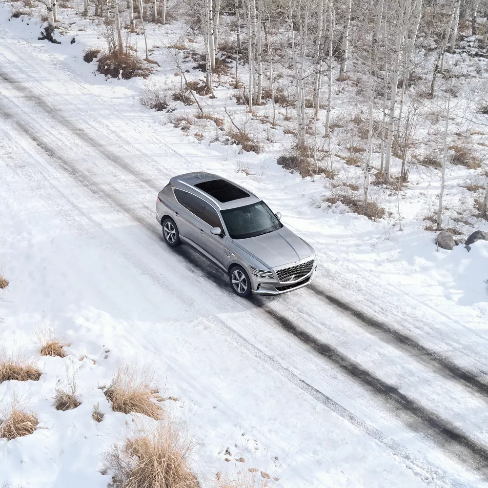 A gray GV80 driving through snowy conditions.