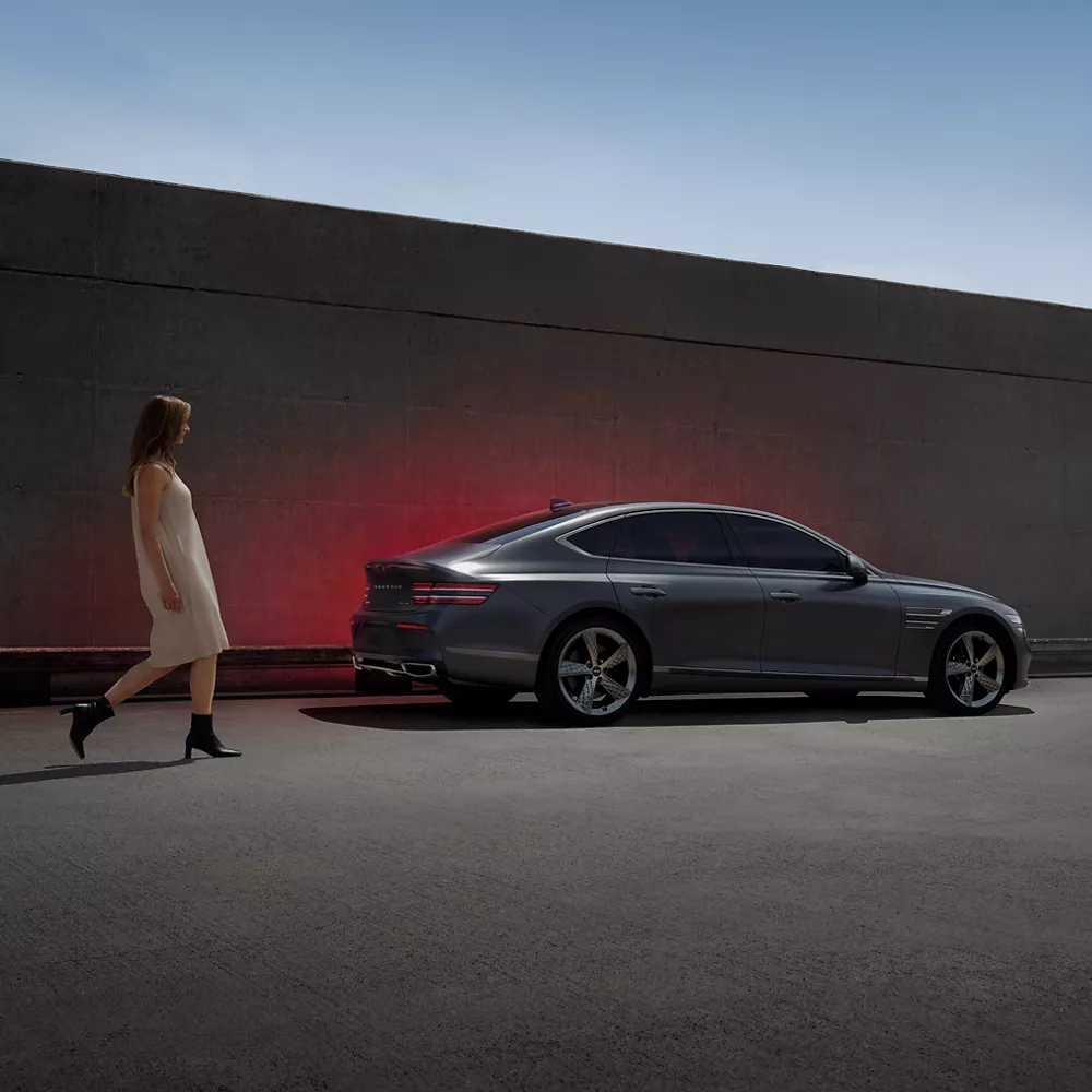 Woman walking next to a G80 parked next to a wall. 