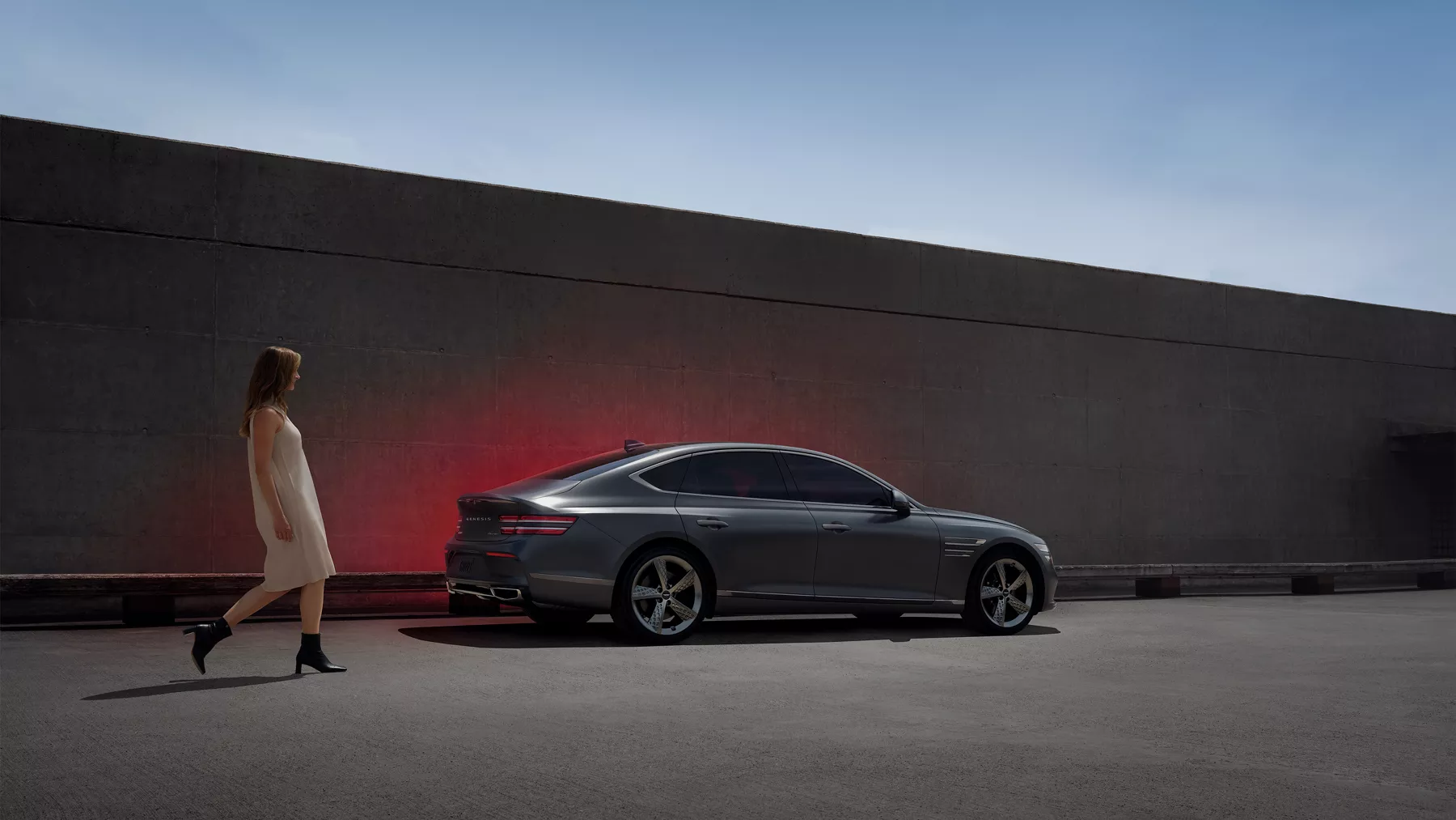 Woman walking next to a G80 parked next to a wall. 