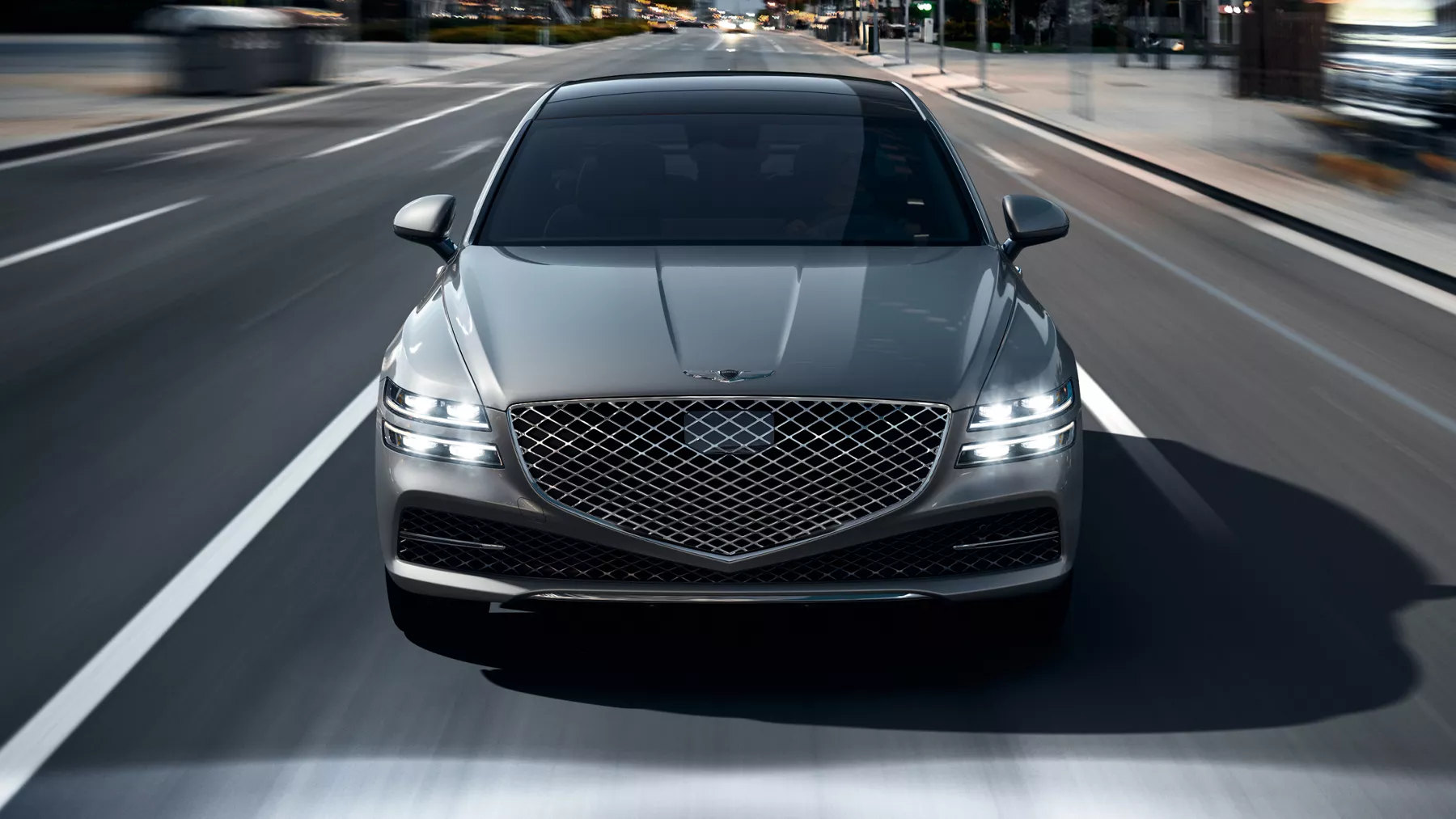 G80 with headlights on driving on a city highway.