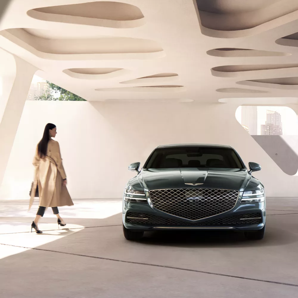 Mujer caminando junto a un G80 estacionado junto a una obra de arte estructural blanca.