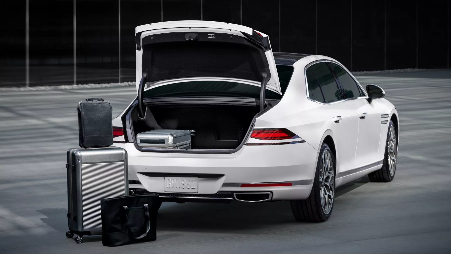 G90 opened trunk with suitcases stacked on ground beside vehicle.