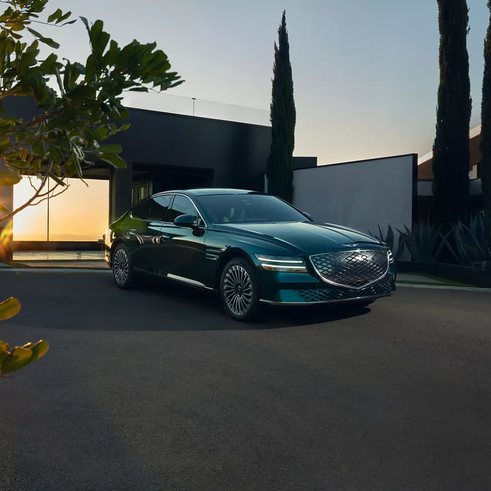 Electrified G80 sitting in the driveway with open garage behind it.