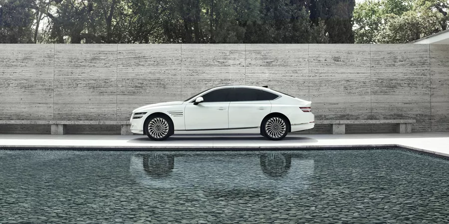 Side profile of White Electrified G80 parked beside a reflecting pool.