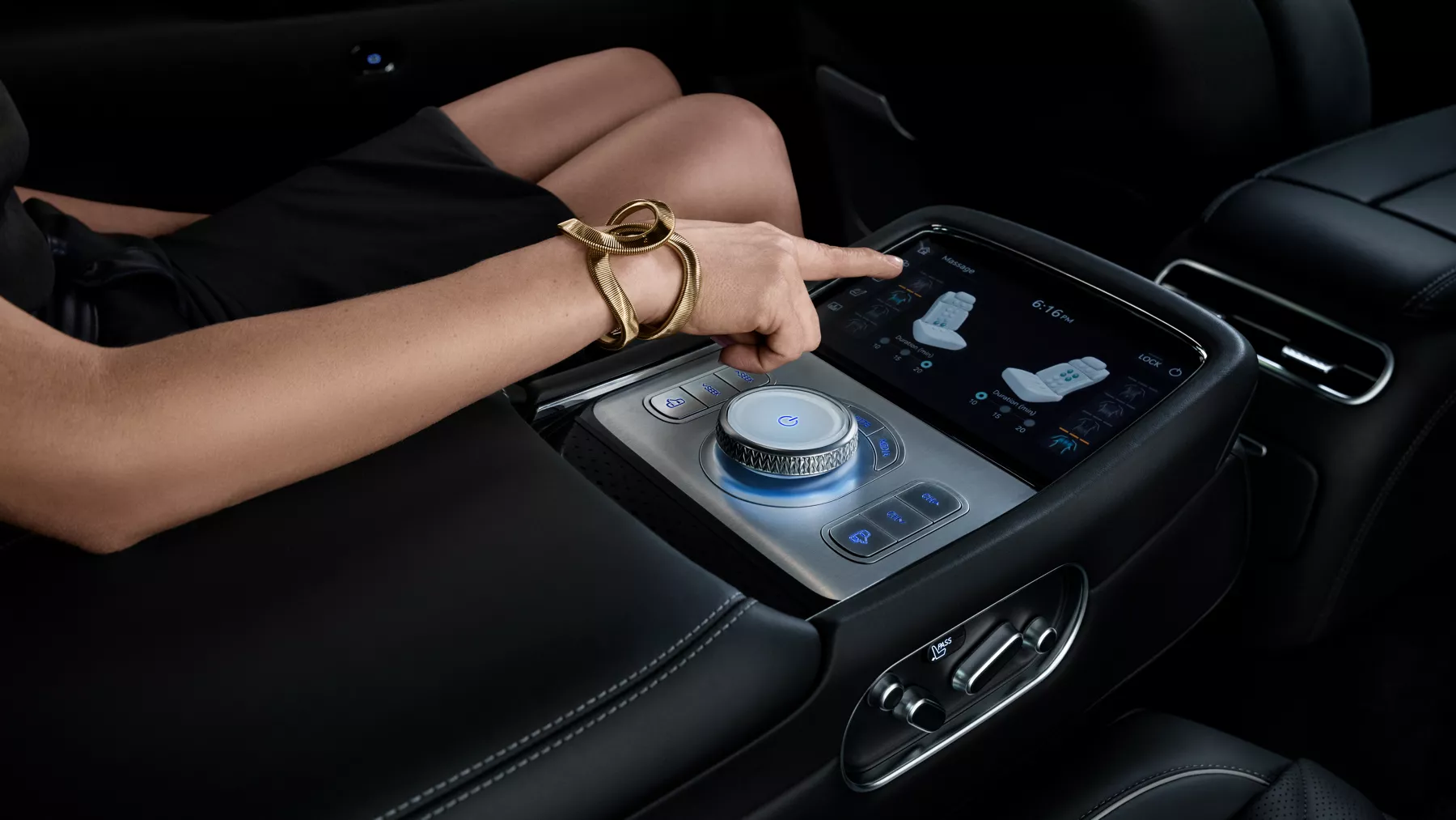 Elegantly-dressed woman sitting in G90 driver's seat and adjust seat position with center console touchscreen controls.