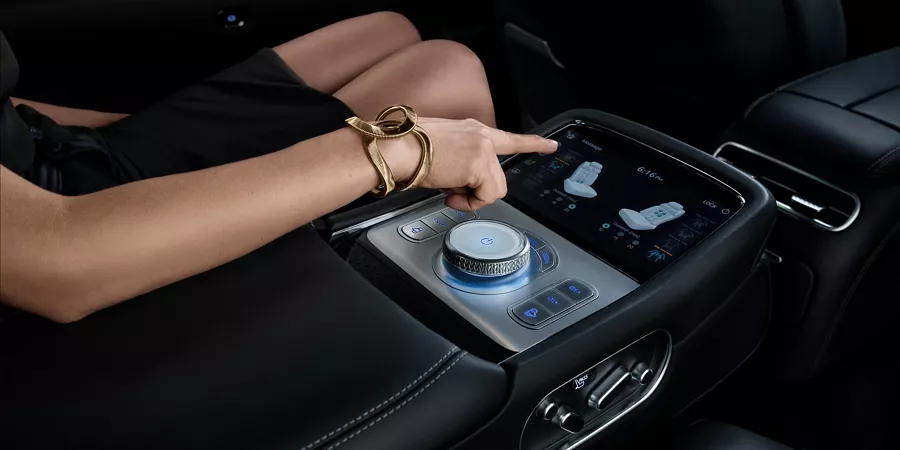Elegantly-dressed woman sitting in G90 driver's seat and adjust seat position with center console touchscreen controls.