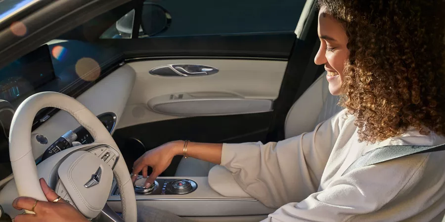 Mujer sentada en el asiento del conductor del Electrified GV70 sosteniendo el volante y ajustando el dial de la consola central.