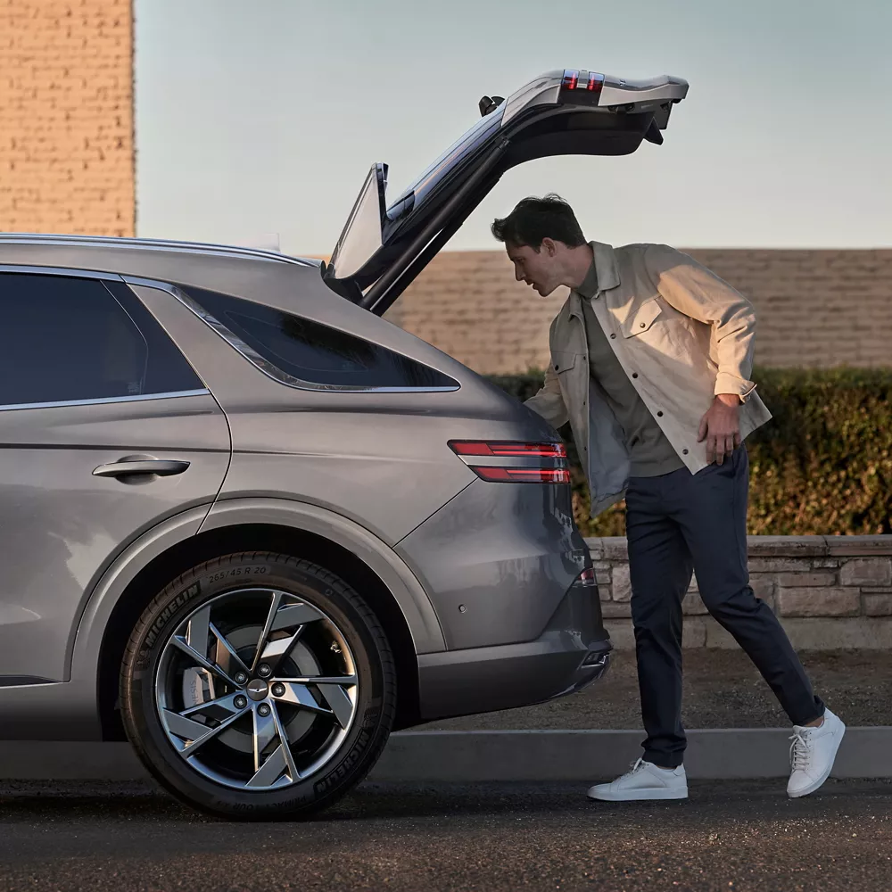 Electrified GV70 trunk door opened with man looking inside trunk.