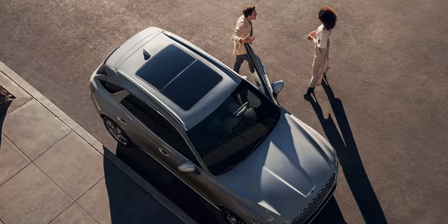 Two people standing outside of a parked Electrified GV70 with a sunroof.