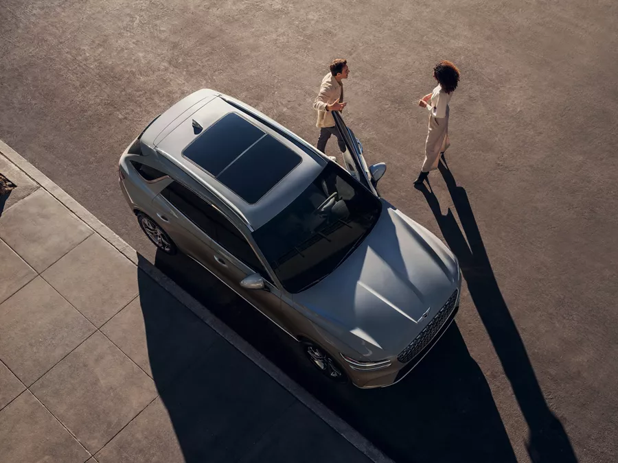 Two people standing outside of a parked Electrified GV70 with a sunroof.