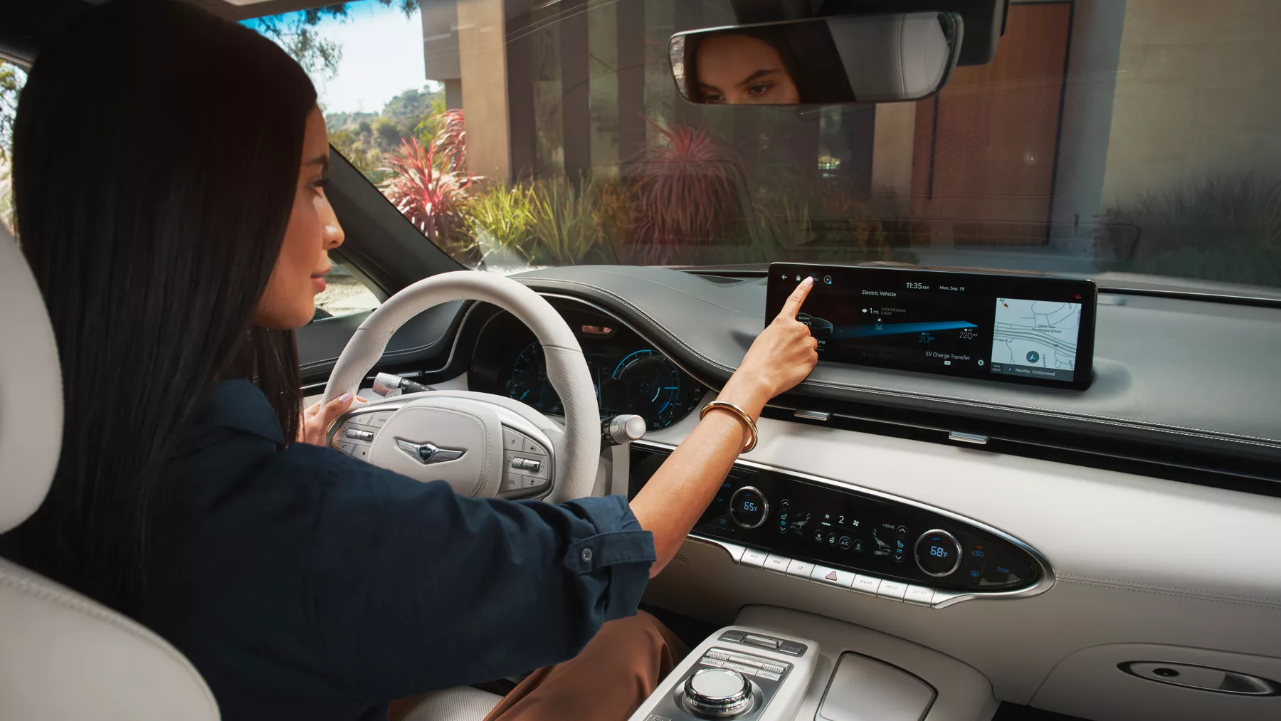 Woman seated in Electrified GV70 driver's seat, touching infotainment screen screen.