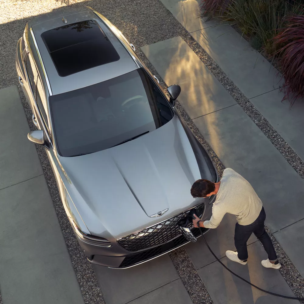 Electrified GV70 parked in driveway with man plugging an electric charger into front of vehicle. 