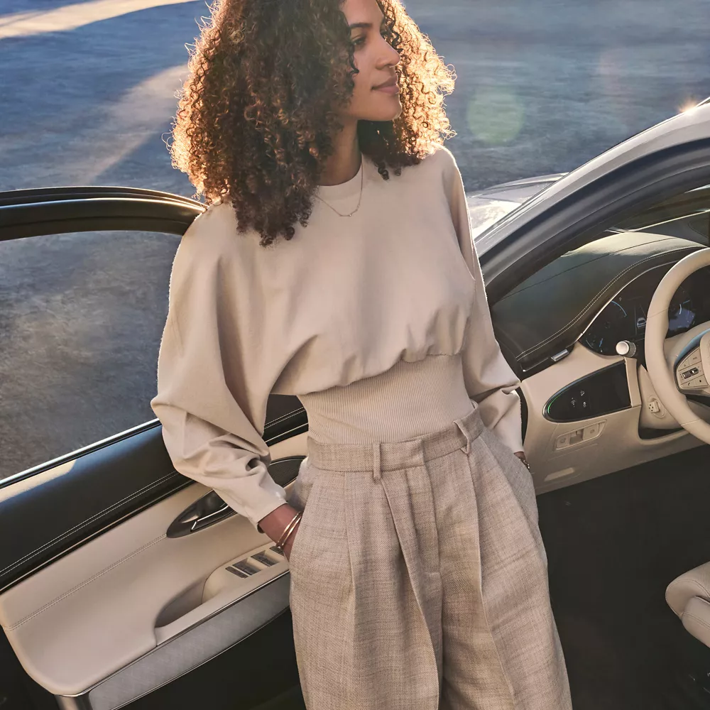 Woman standing next to Electrified GV70 with driver's-side front door open.