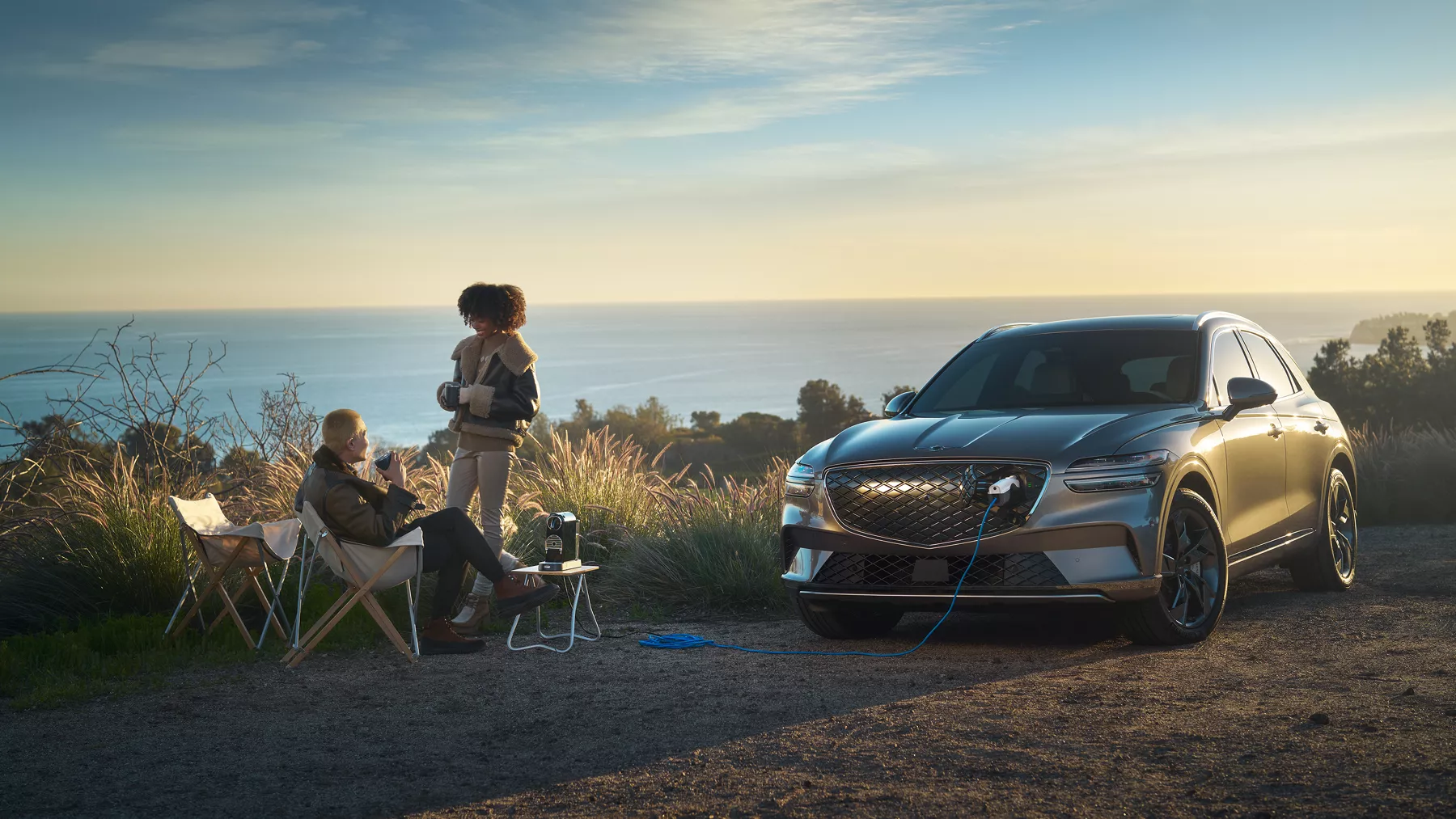 Two people charging their devices using the Electrified GV70 while camping.