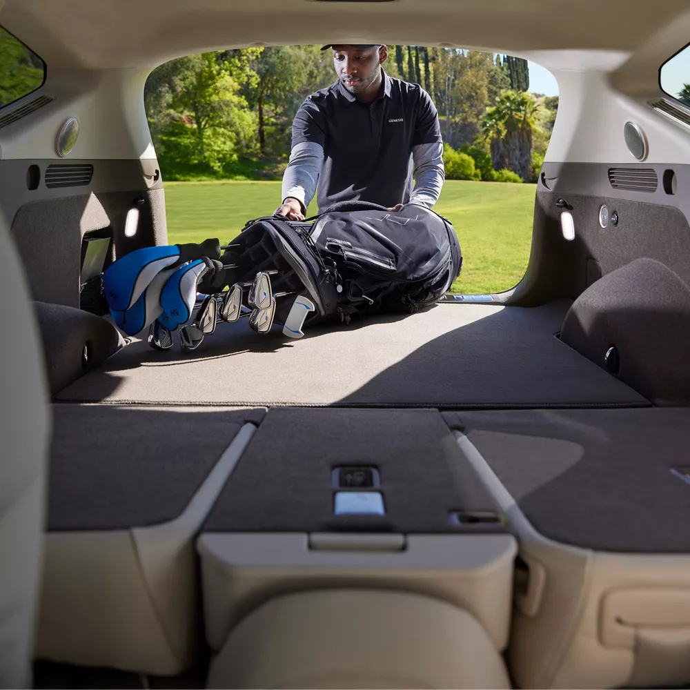 Man loading a set of golf clubs in the rear of a GV80 with rear seats folded down.