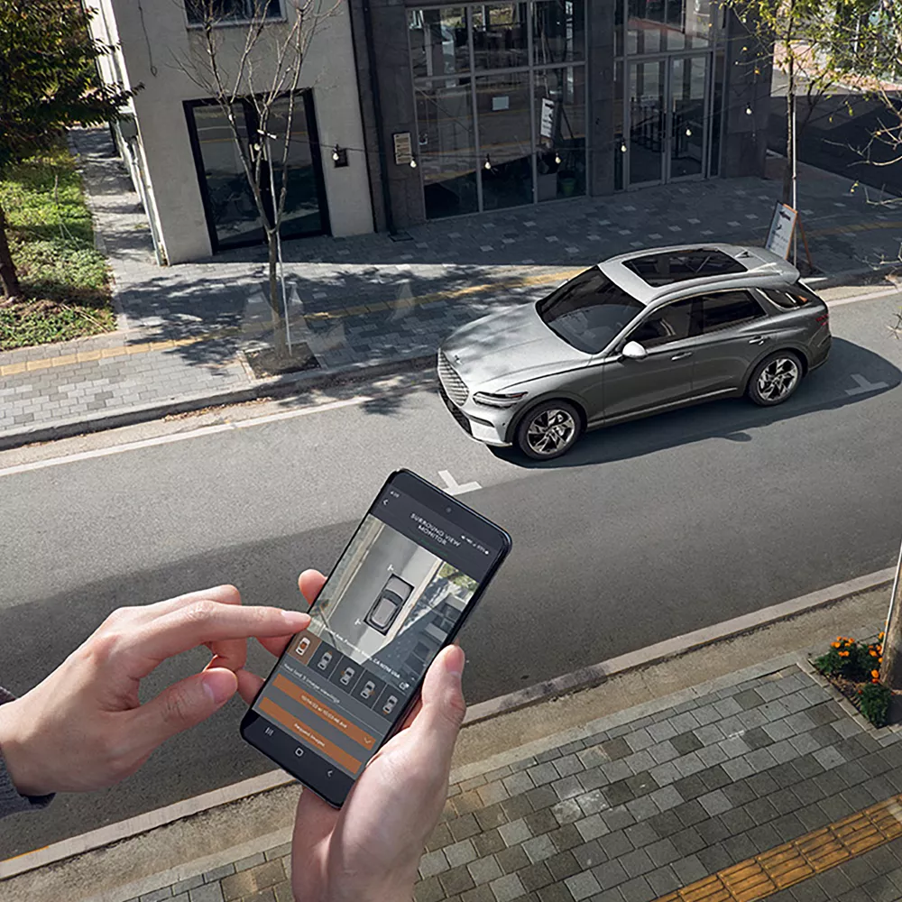 Persona mirando un teléfono inteligente en el que se muestra la imagen de un Electrified GV70 estacionado en la calle de una ciudad.