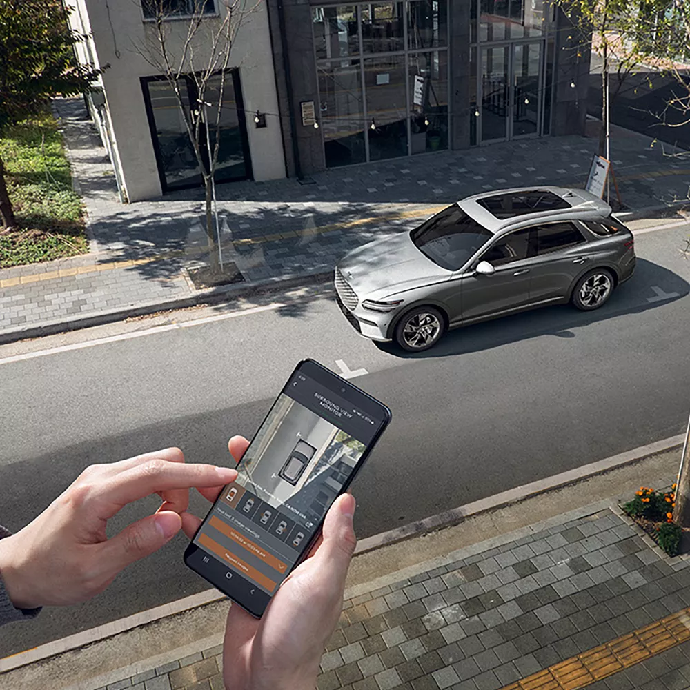 Person looking at smartphone displaying image of an Electrified GV70 parked on a city street.