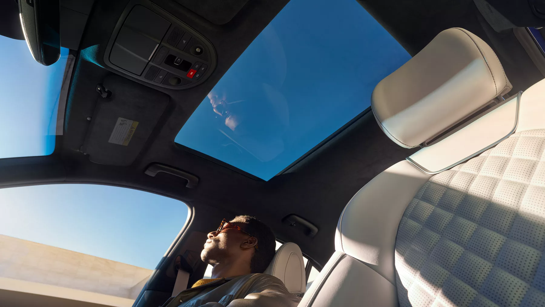 Upward view of G70 front cabin and sunroof with man in passenger seat.