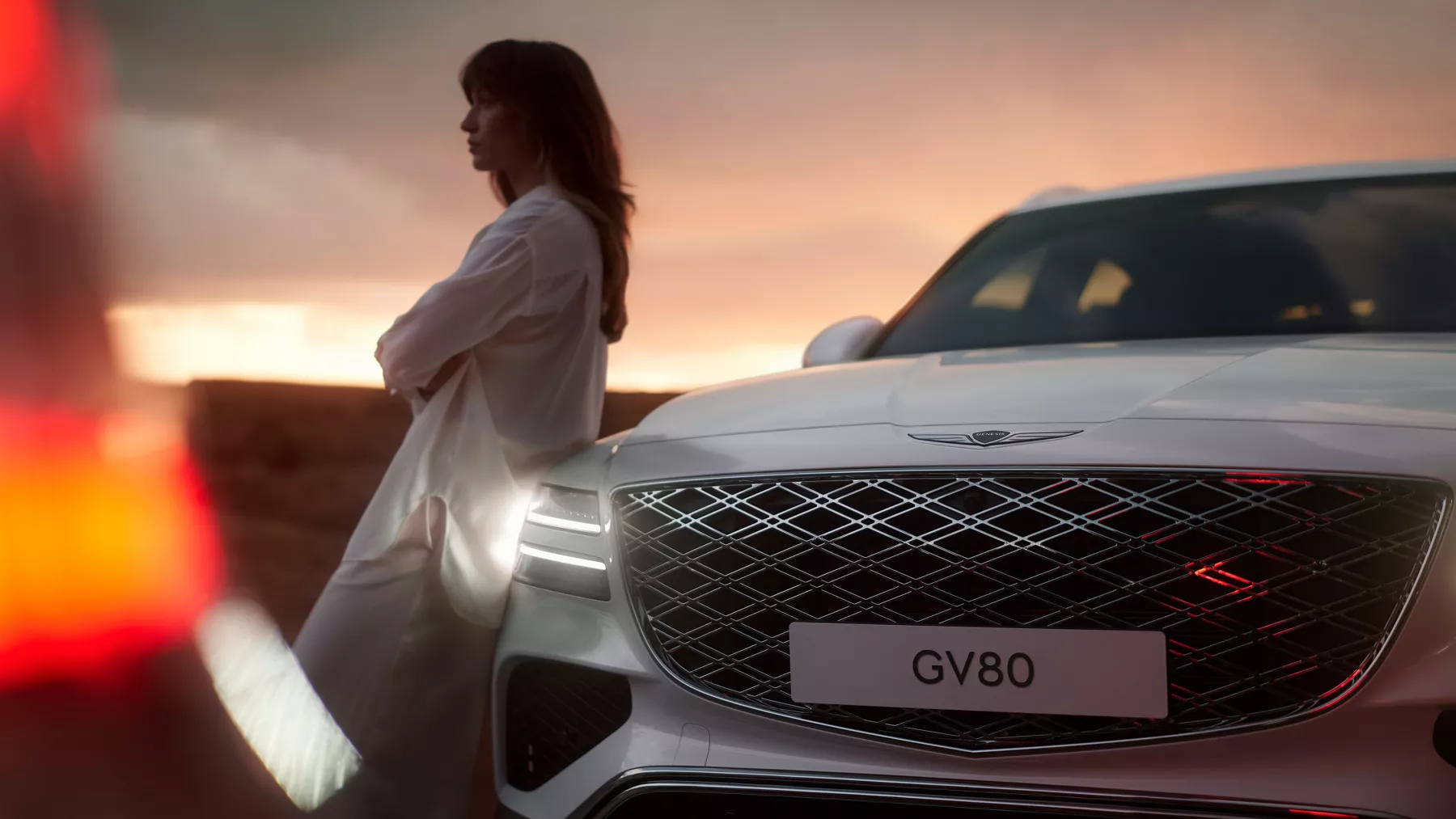 Front grille of GV80 with a woman leaning against the vehicle hood.